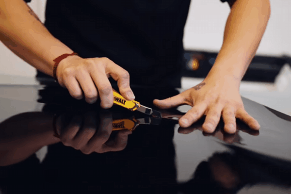 A technician carefully cutting and applying window tint film to a car surface with precision tools. The close-up shot highlights the attention to detail and expertise involved in professional window tint installation.